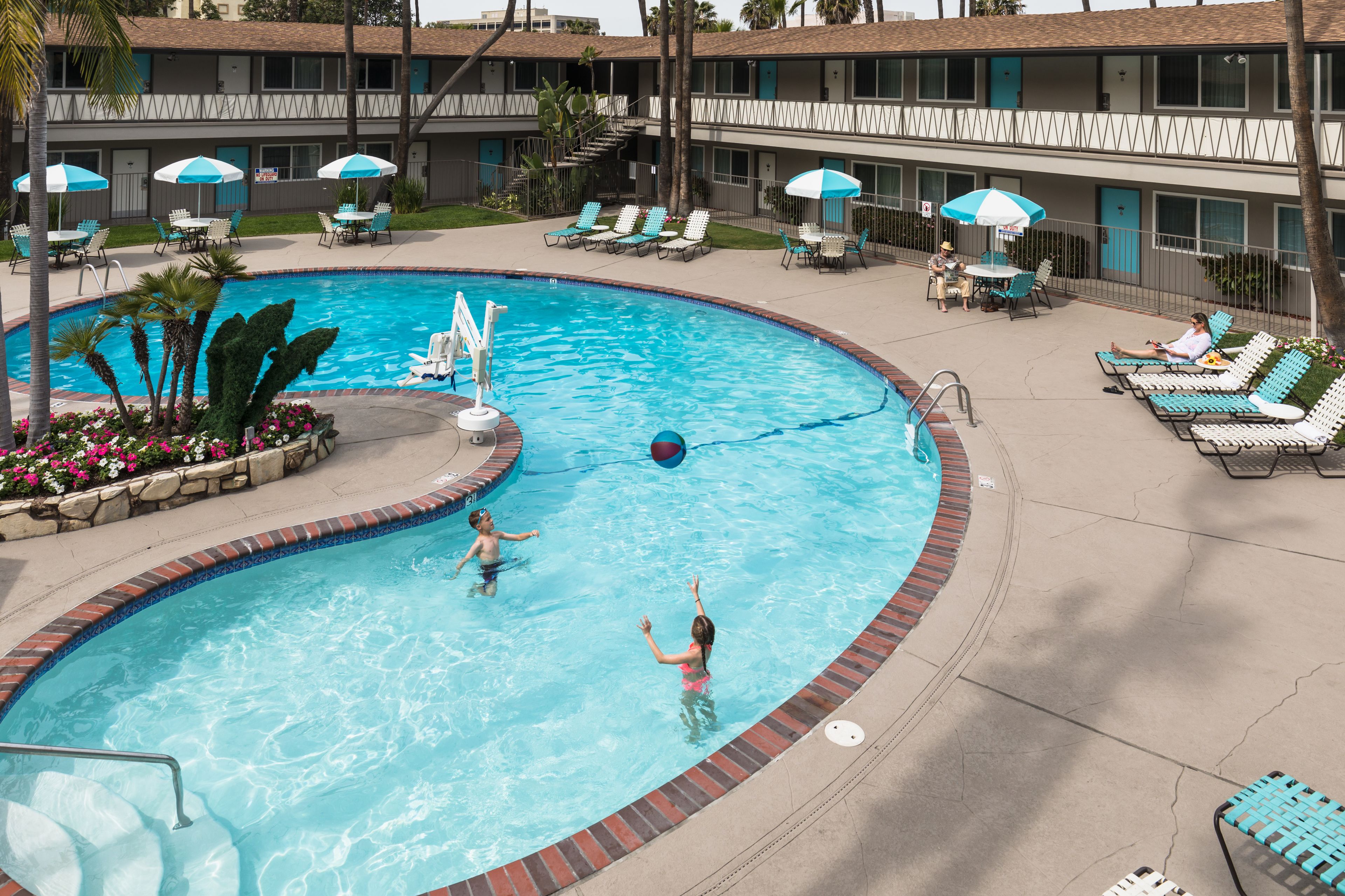 A swimming pool with lounge chairs and umbrellas, surrounded by a building with a tiled roof and a staircase.