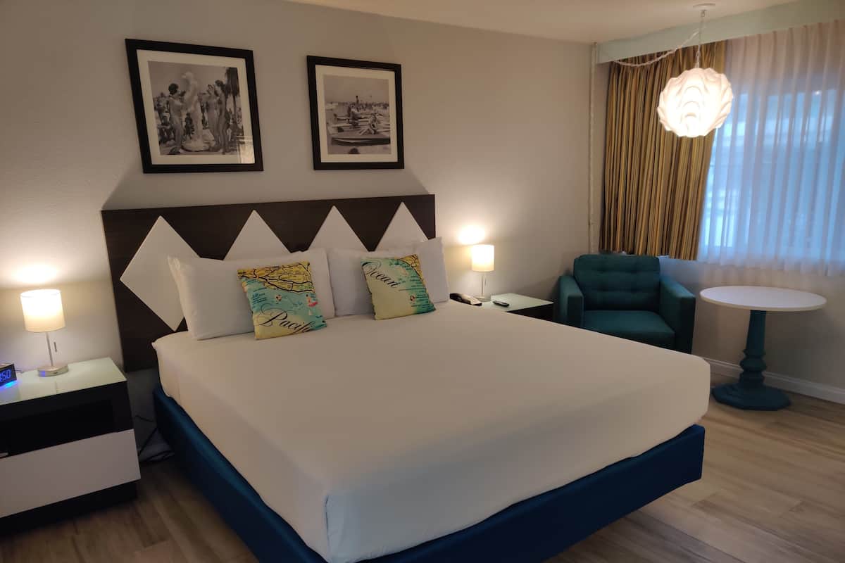 A hotel room with a large bed, two nightstands, a desk, a chair, and a round table. There are two framed pictures on the wall above the bed.