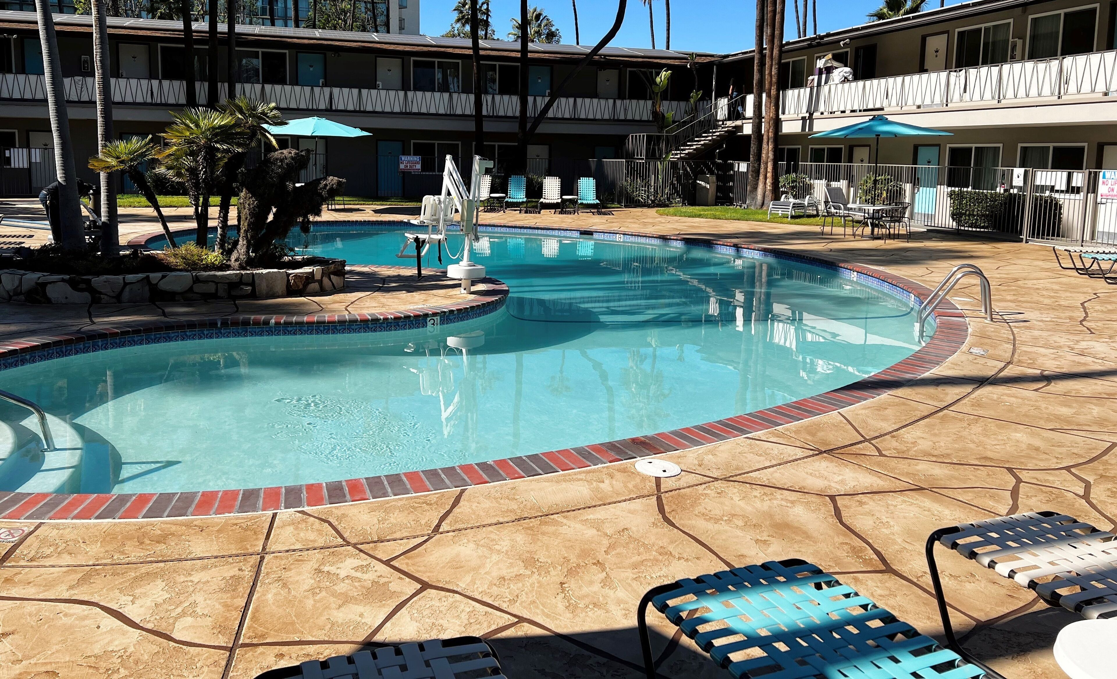 A swimming pool with a tiled edge, lounge chairs, and a building with balconies in the background.