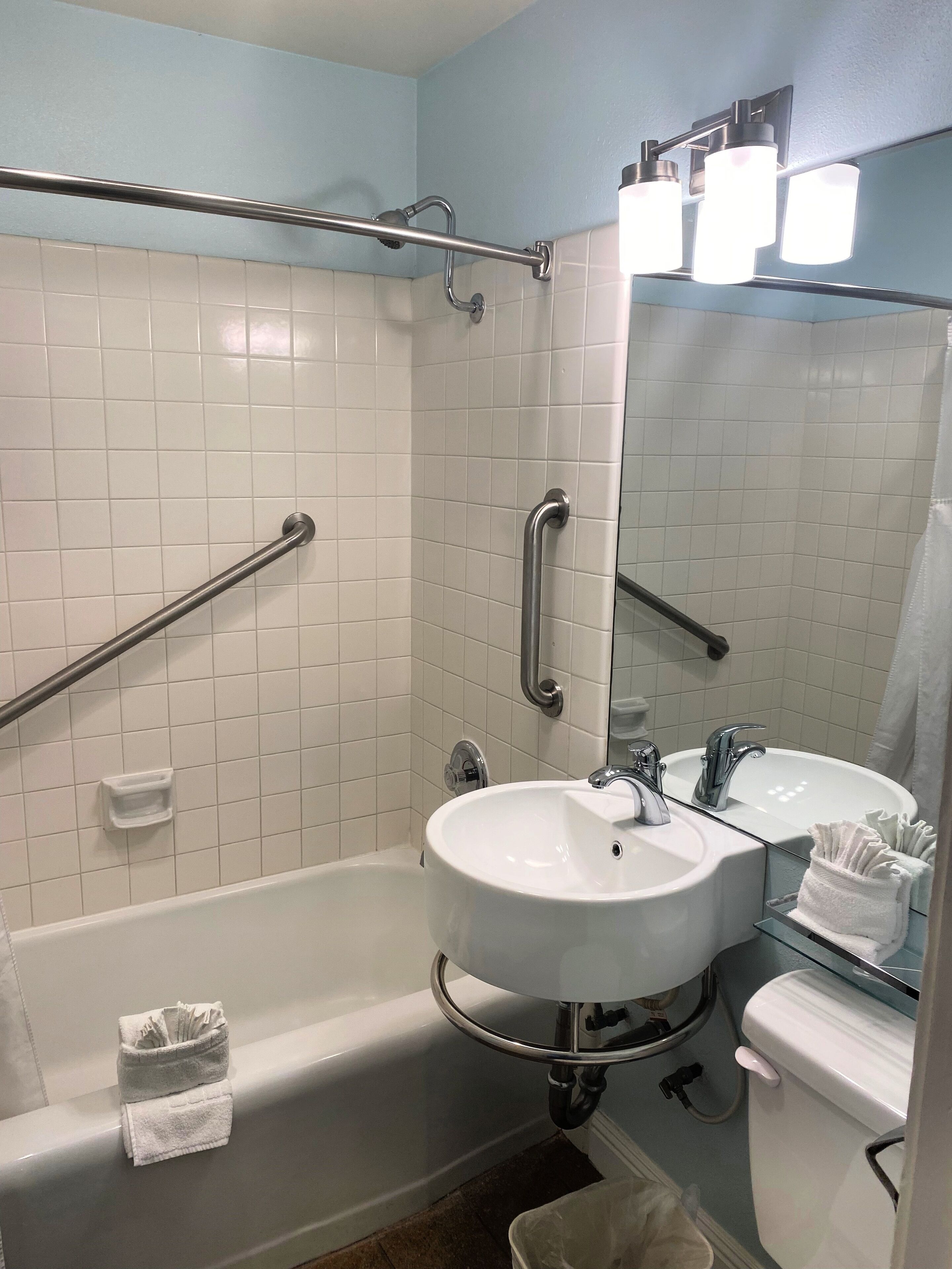 Een badkamer met witte tegels, een bad, een wastafel, een toilet en een spiegel.