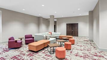 Un hall d’hôtel doté d’un espace détente comprenant des canapés, des fauteuils et des poufs, ainsi qu’une moquette à motifs et une porte en bois.