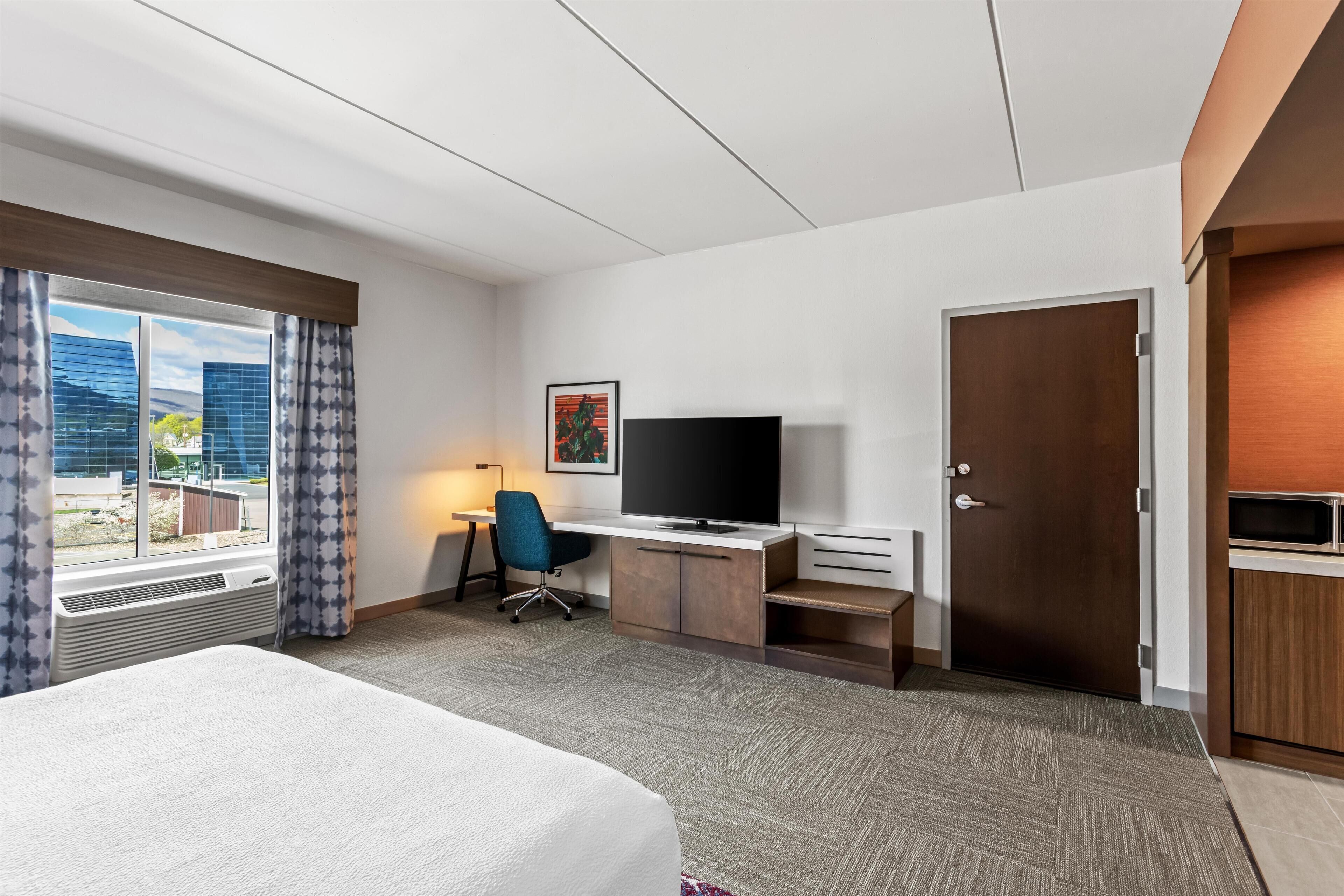 A hotel room with a bed, desk, TV, and a view of the city.