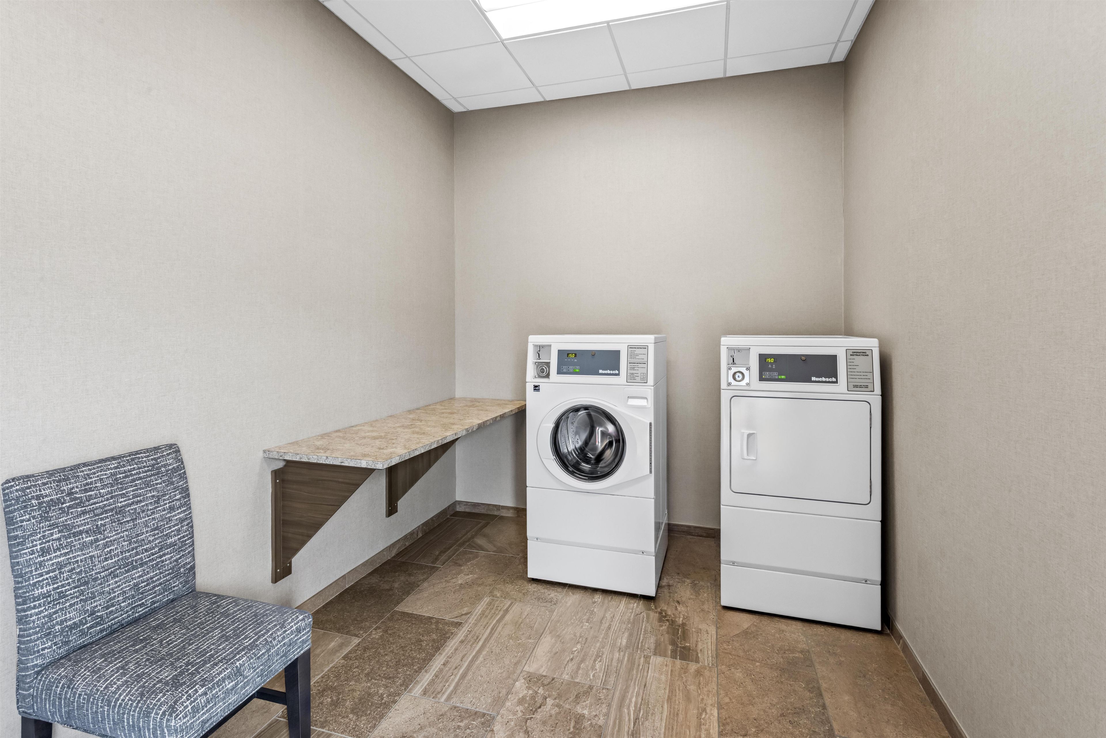 A laundry room with two stacked front-loading washing machines, a bench, and a tiled floor.