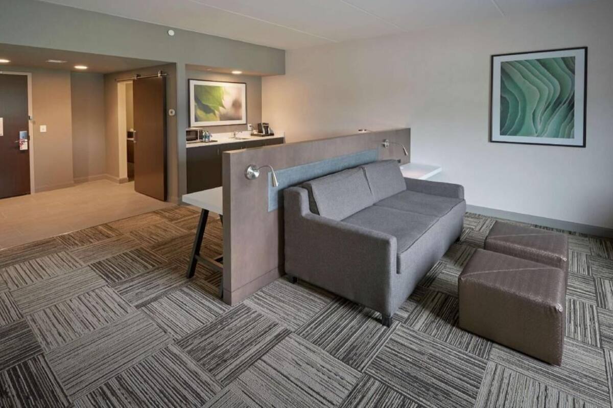 Ein Hotelzimmer mit einer Couch, Hocker und einem Schreibtisch mit Stuhl.