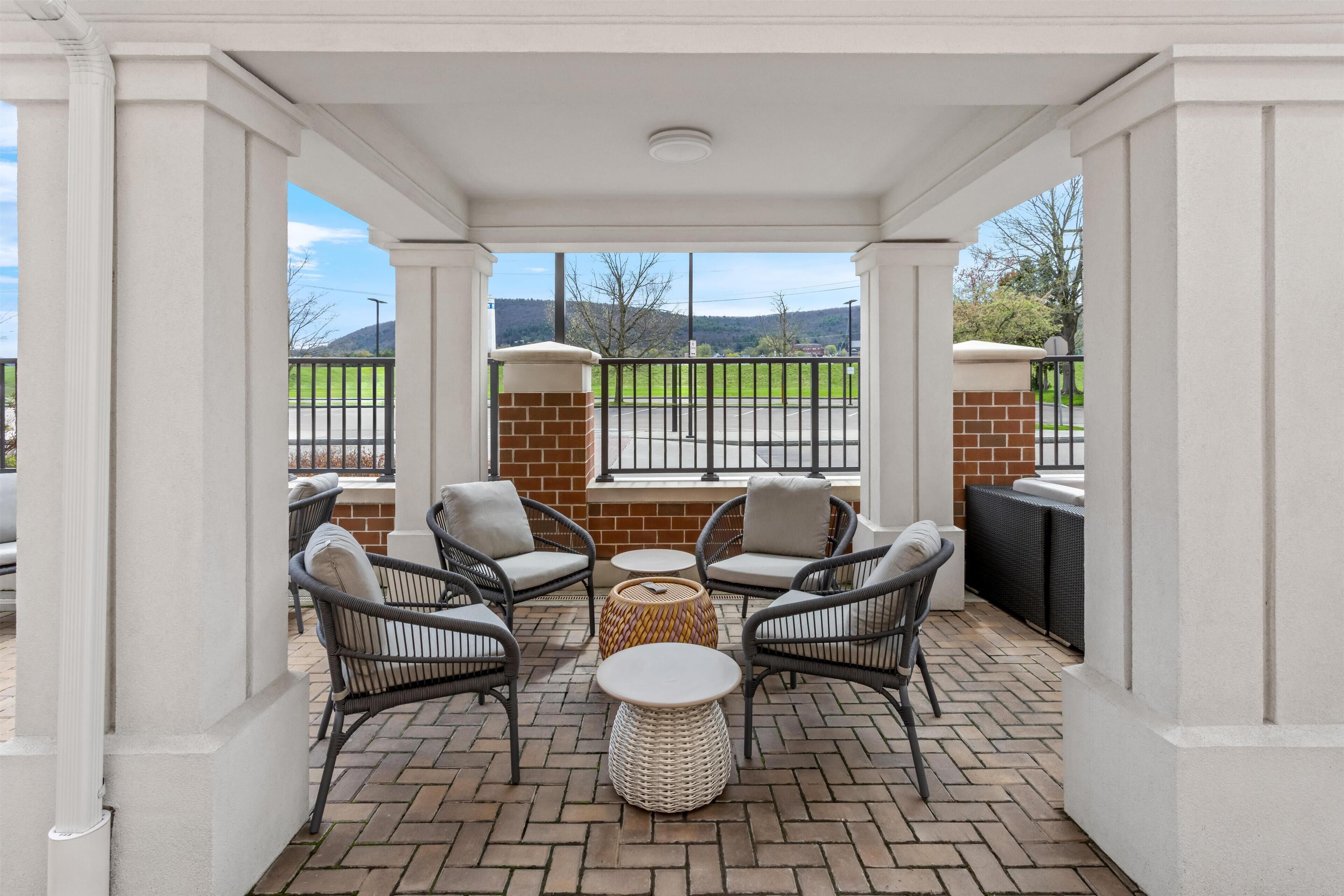 A covered patio with wicker chairs, a round table, and a view of a green field.