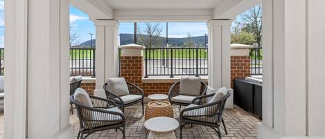 A covered patio with wicker chairs, a round table, and a view of a green field.
