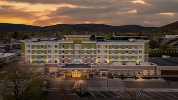 Un hôtel à plusieurs étages, doté d’une entrée imposante, d’un parking et offrant une vue sur les collines environnantes.
