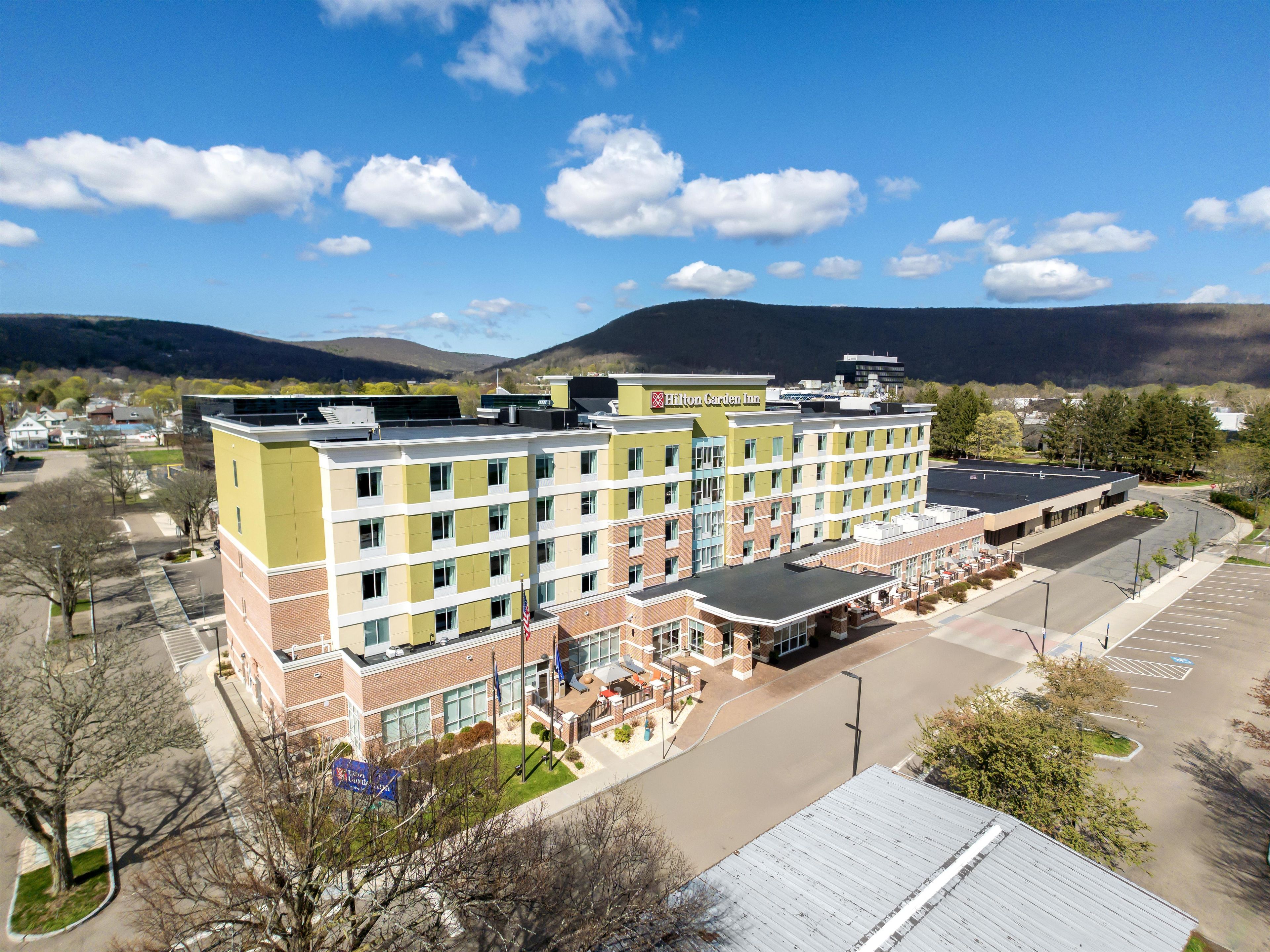 A multi-story hotel with a flat roof, a parking lot, and a view of the surrounding landscape.