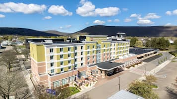 A multi-story hotel with a flat roof, a parking lot, and a view of the surrounding landscape.