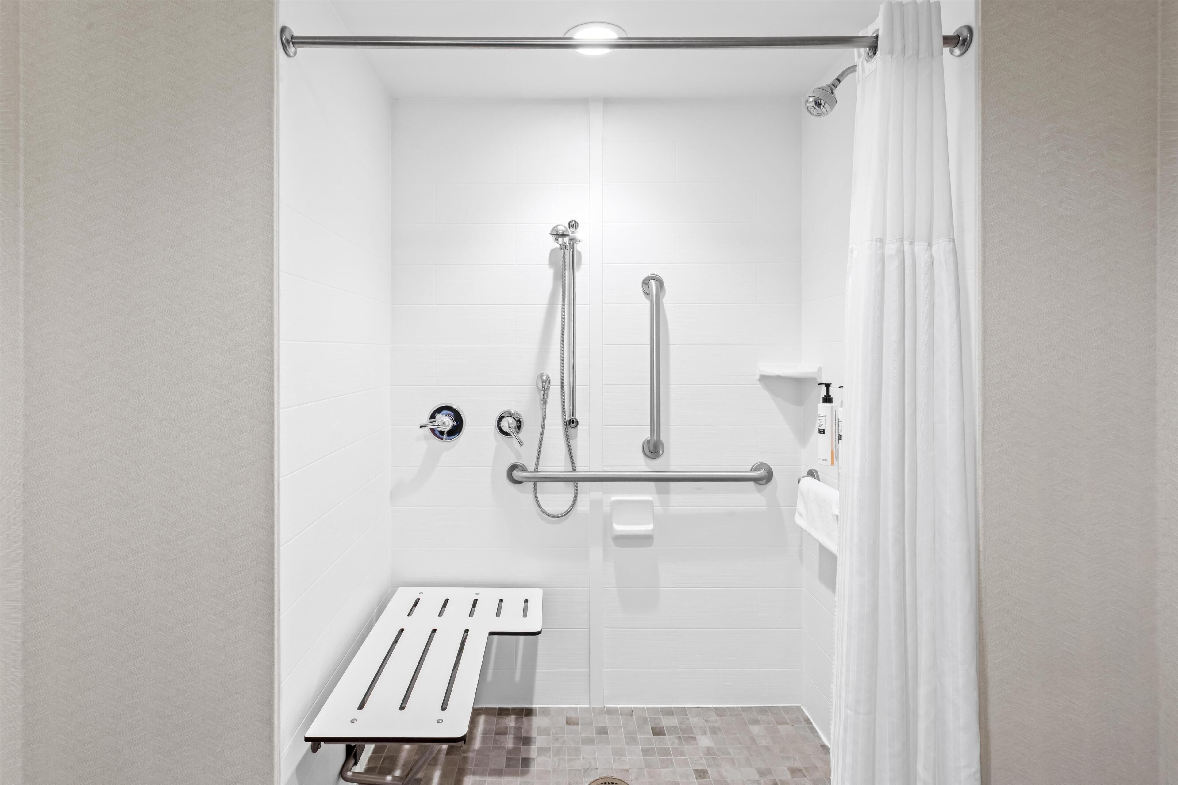 A bathroom with a shower, grab bars, a towel rack, and a toilet paper holder.