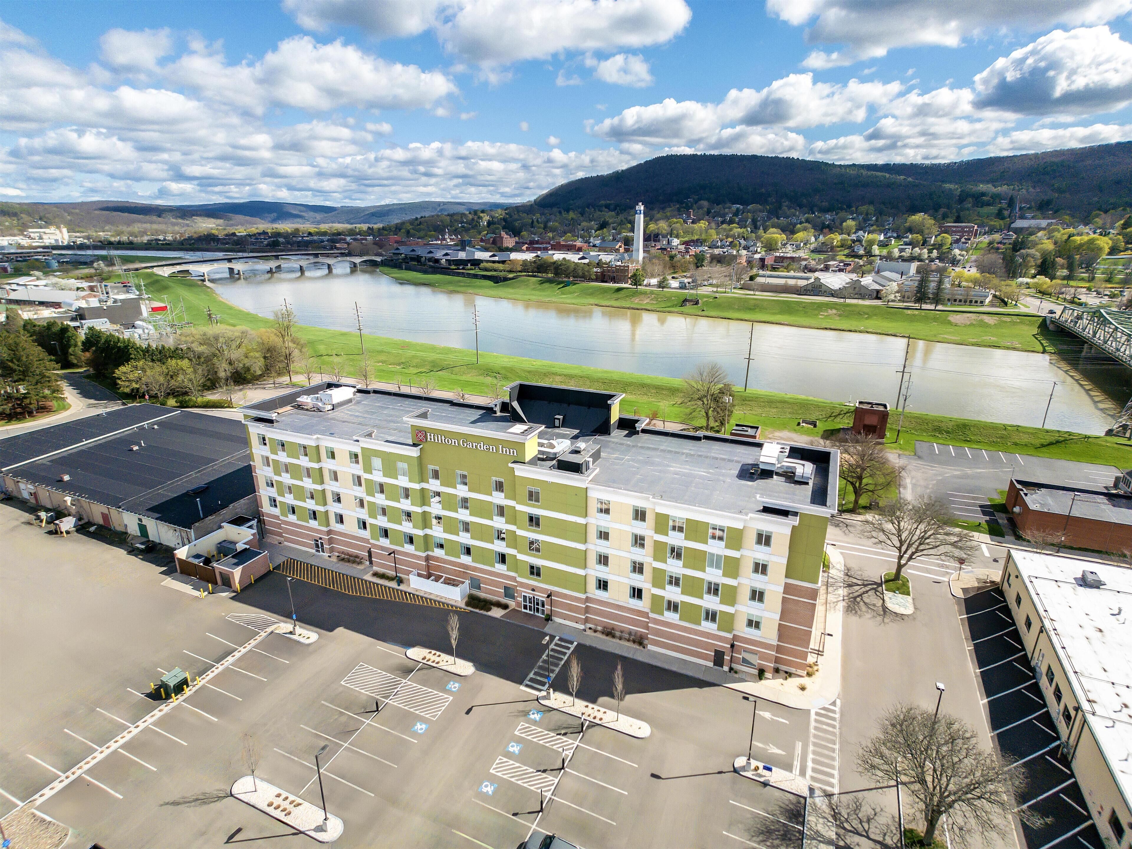 A Hilton Garden Inn with a parking lot, a river in the background, and a bridge.