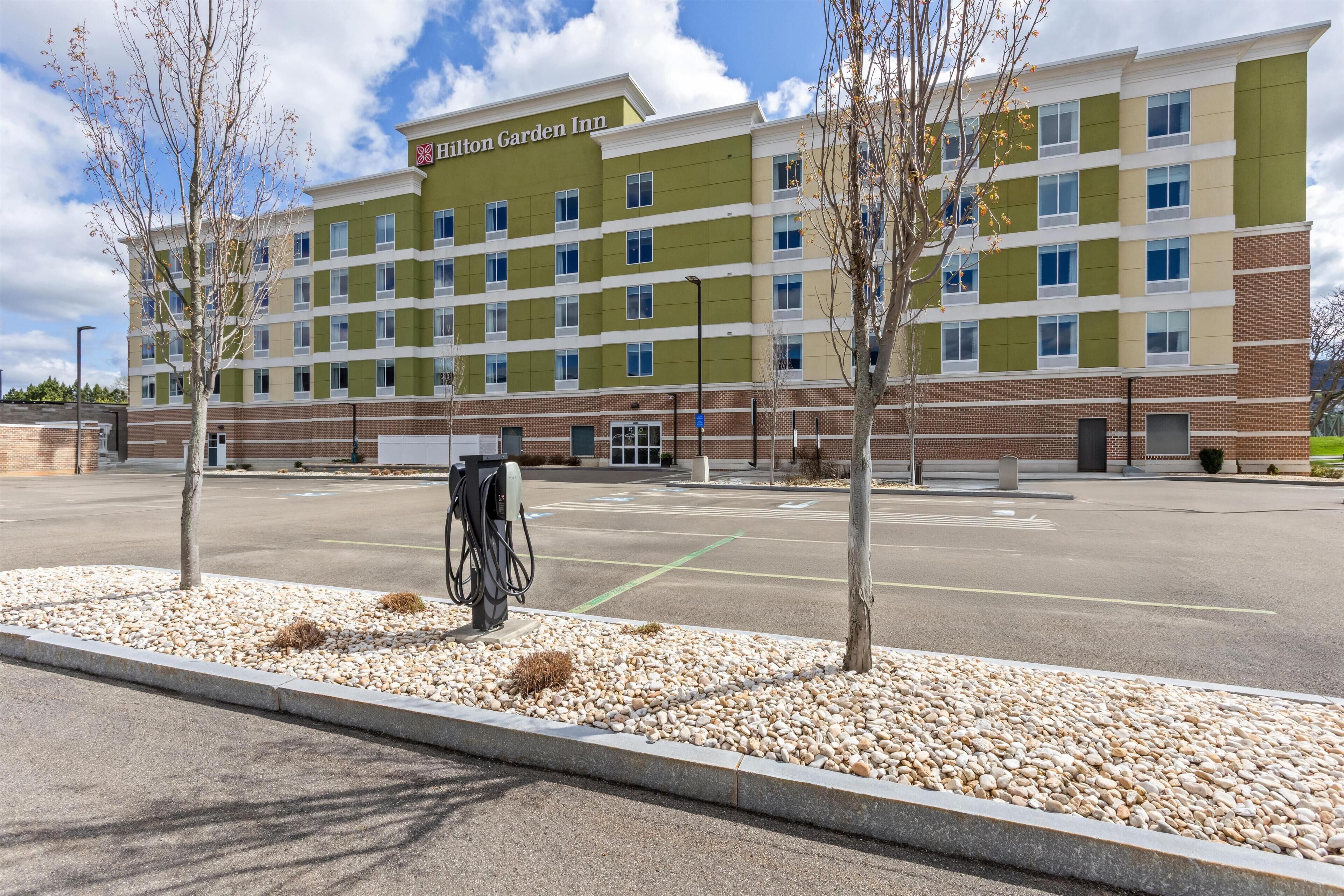 A Hilton Garden Inn with a parking lot, a gas pump, and a row of trees.