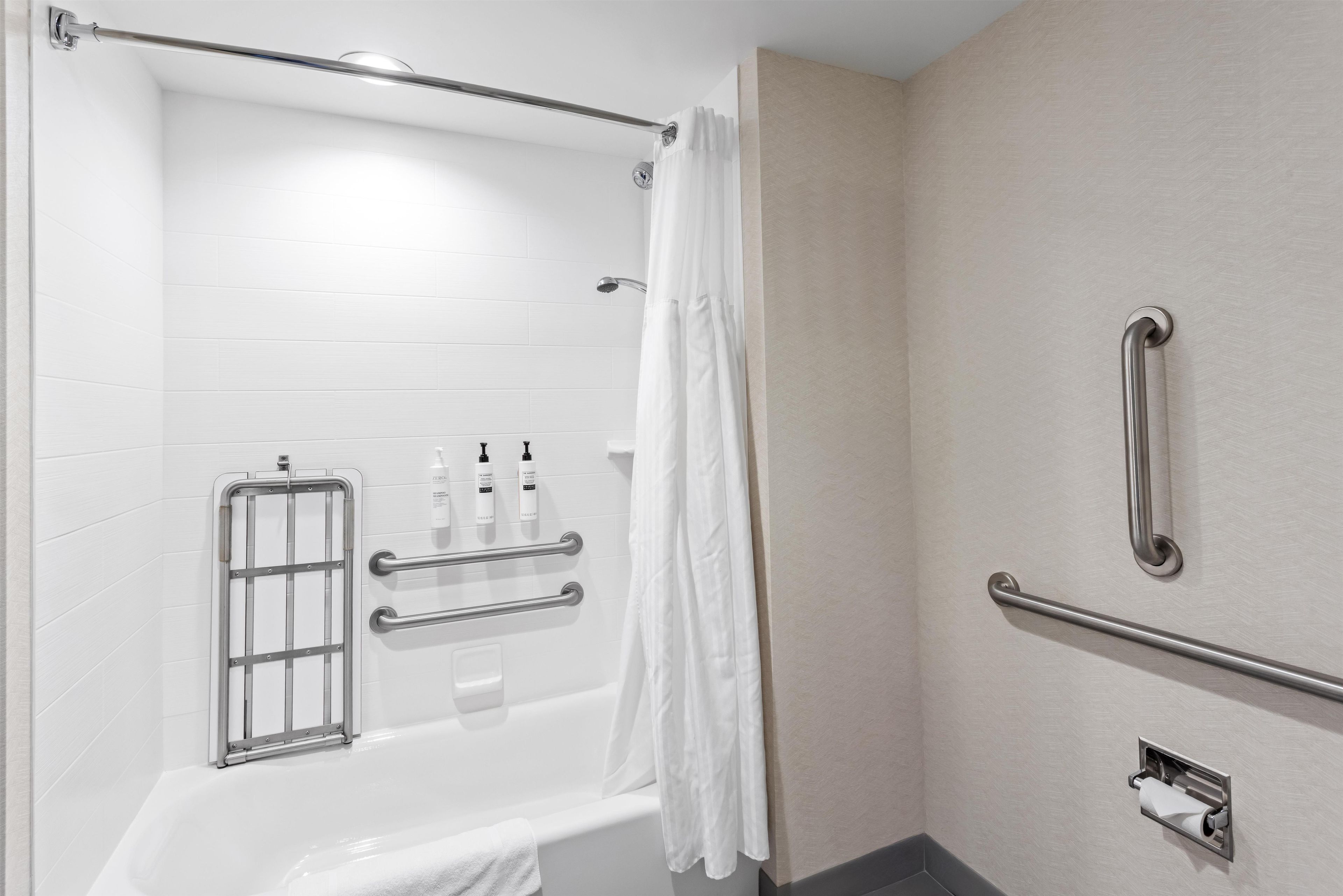 A modern bathroom with a bathtub, grab bars, and a shower curtain.