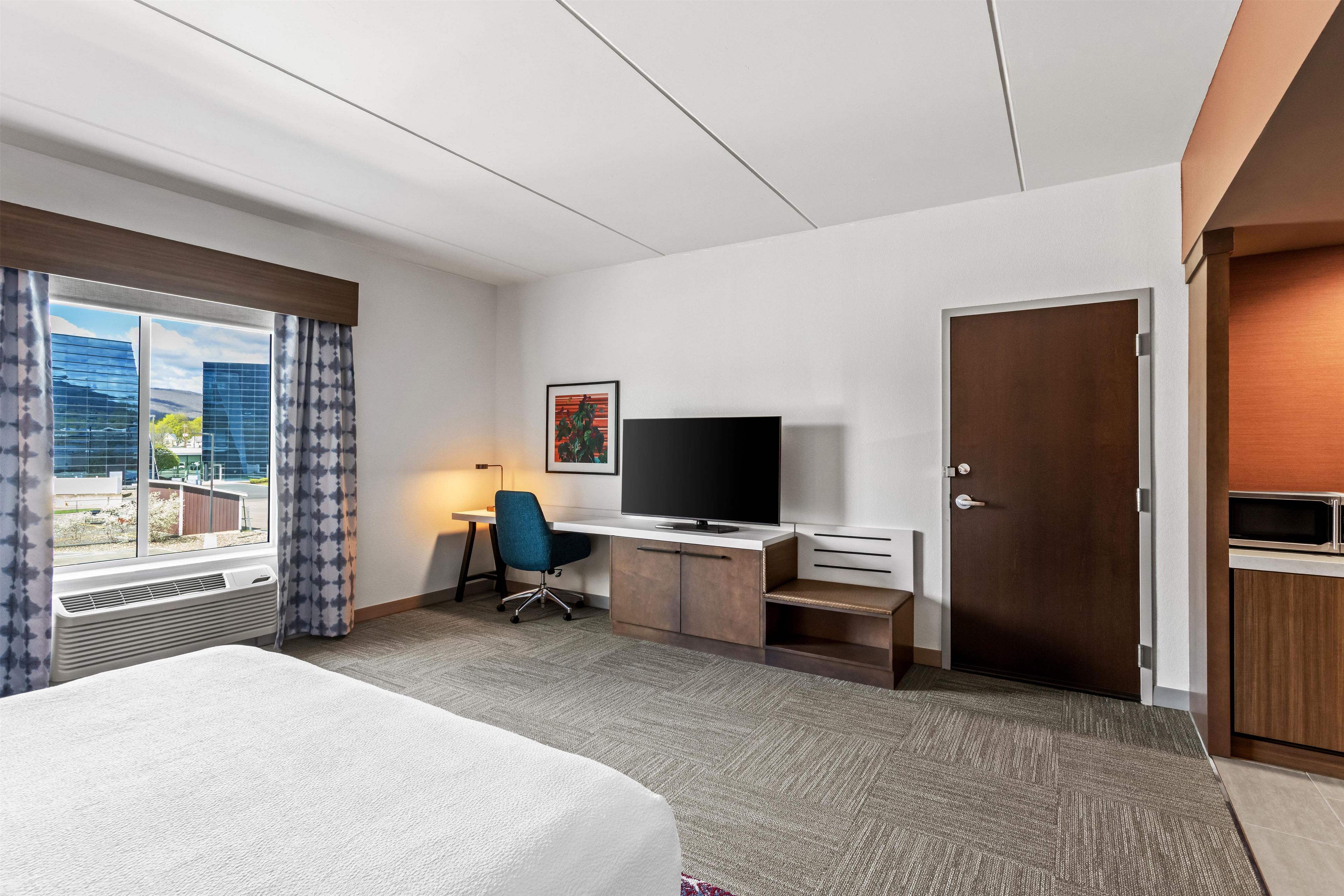 A hotel room with a bed, desk, chair, television, and a door.