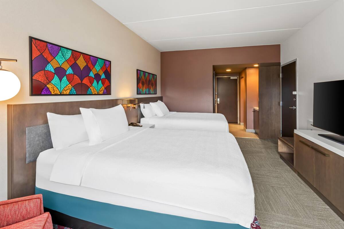 Ein Hotelzimmer mit einem großen Bett, einem Fernseher und Kunstwerken an der Wand.