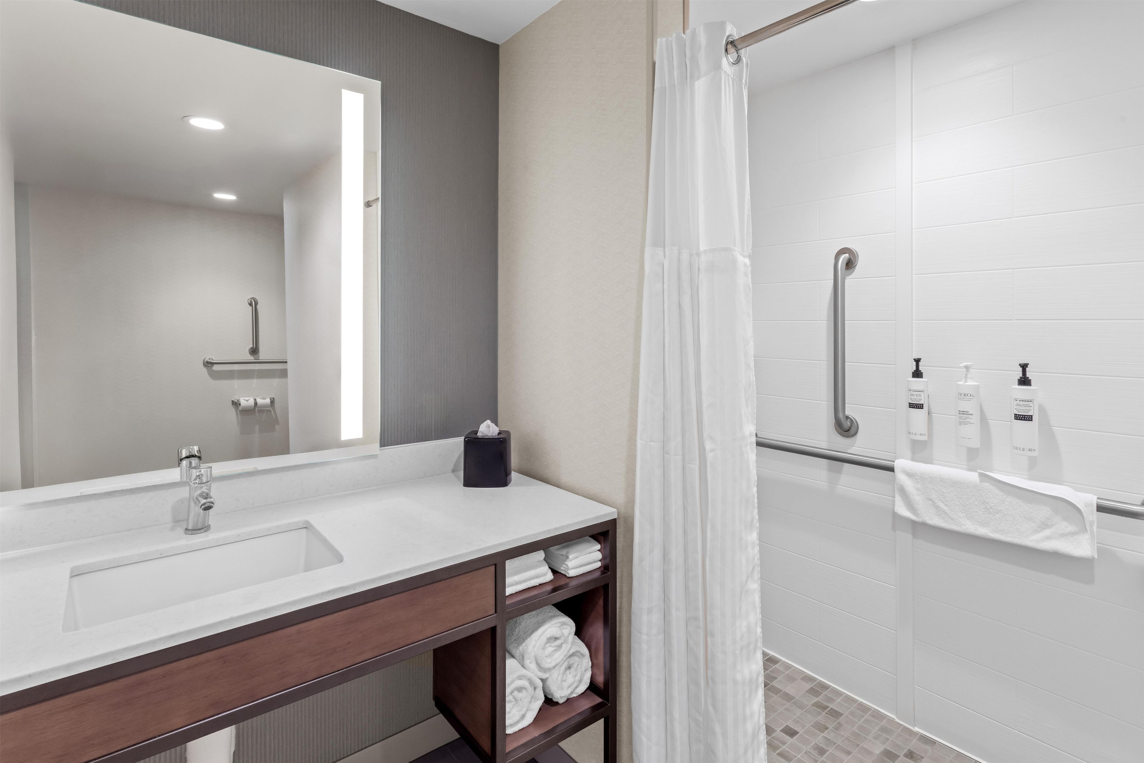 Un baño moderno con un espejo grande, un lavamanos, una ducha con puerta de vidrio y un perchero para toallas.