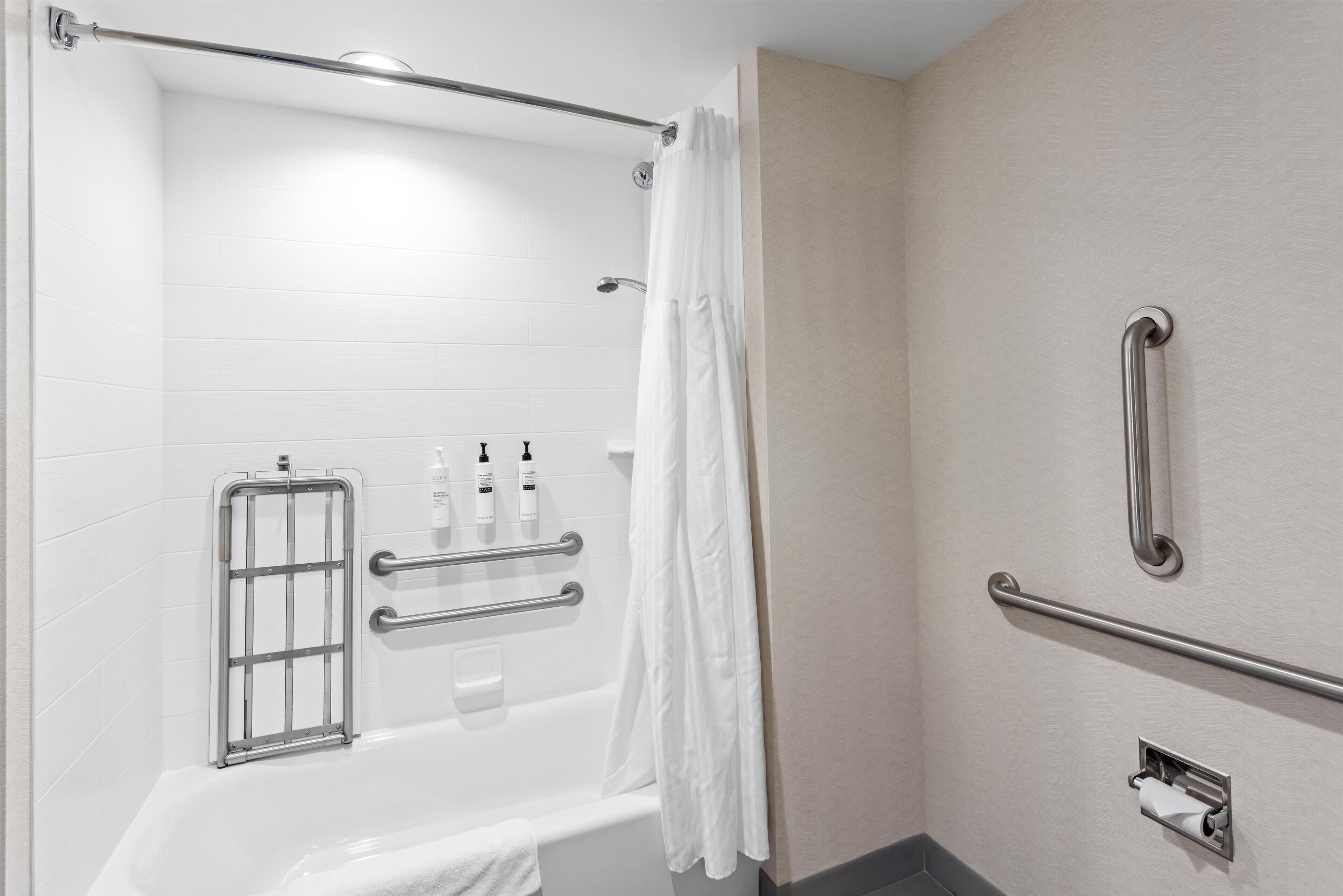A bathroom with a bathtub, grab bars, a shower curtain, and a towel rack.