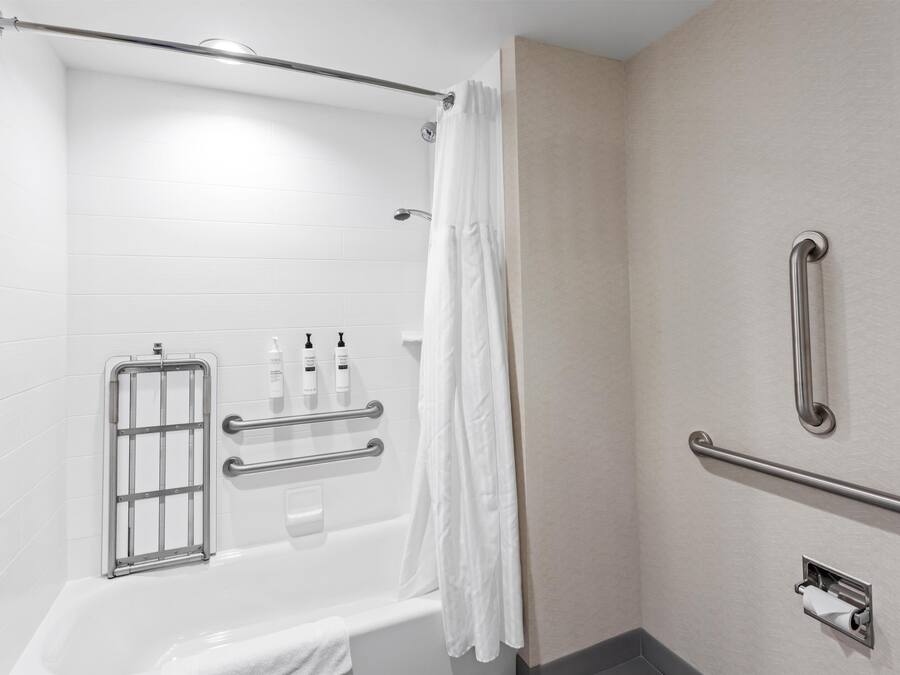 A bathroom with a bathtub, grab bars, a shower curtain, and a towel rack.