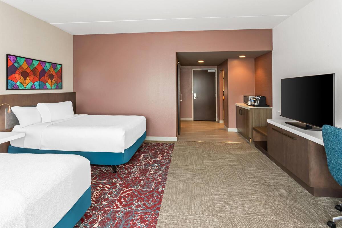 Ein Hotelzimmer mit zwei Betten, einem Fernseher, einem Schreibtisch und einer Mikrowelle.