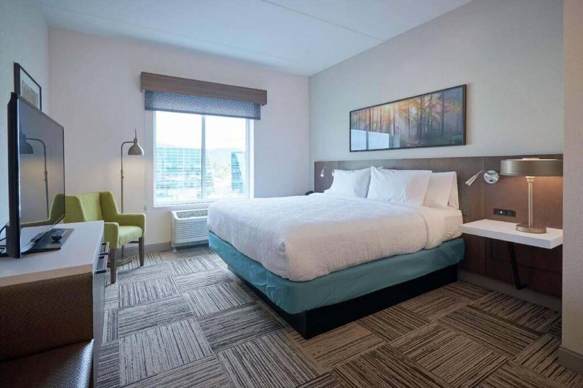 Ein Hotelzimmer mit Bett, Schreibtisch, Stuhl und einem Gemälde an der Wand.
