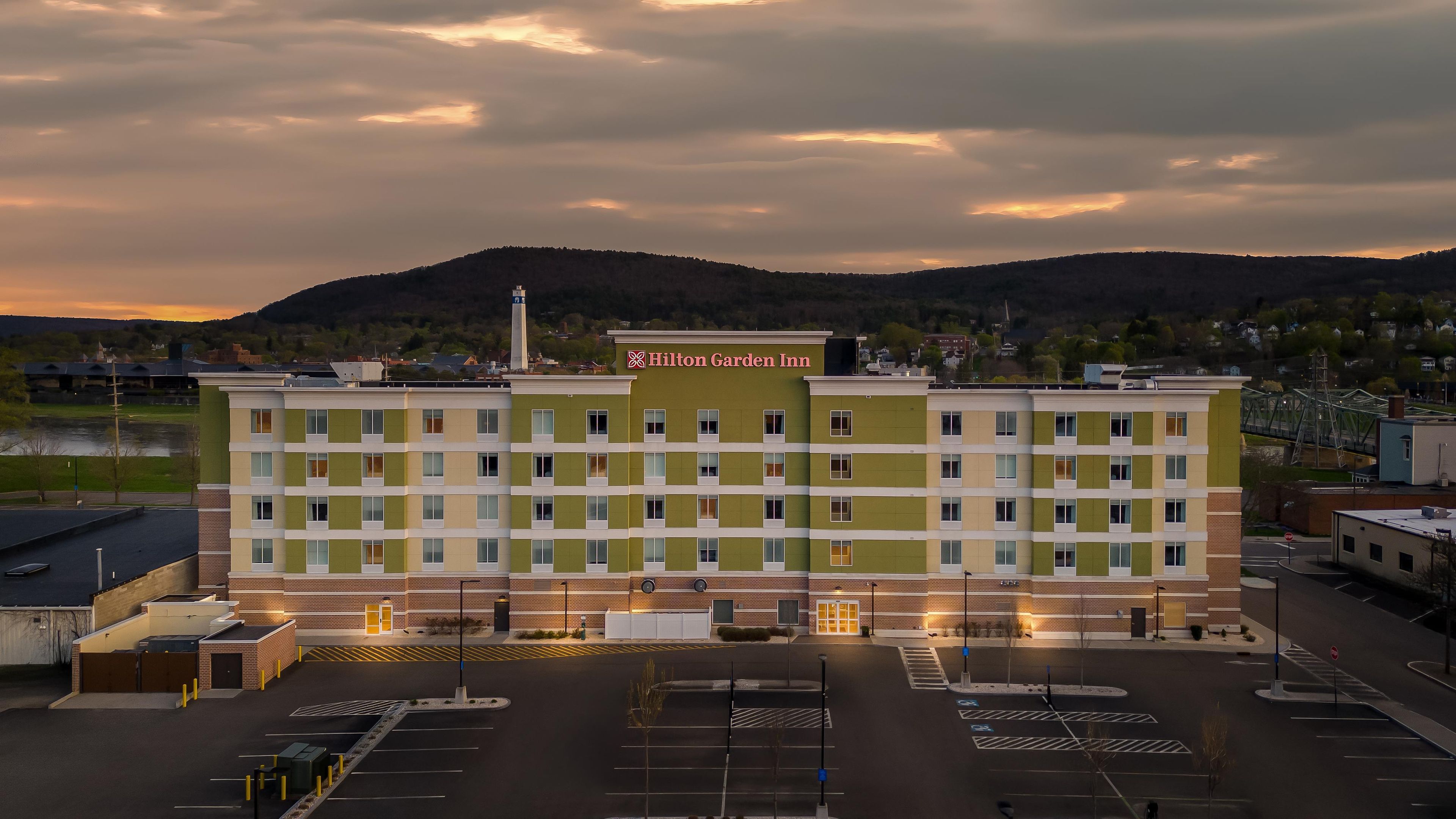 Ein mehrstöckiges Gebäude mit einer grün-beigen Fassade, einem gut sichtbaren Schild des Hilton Garden Inn und einem Parkplatz mit markierten Stellplätzen.