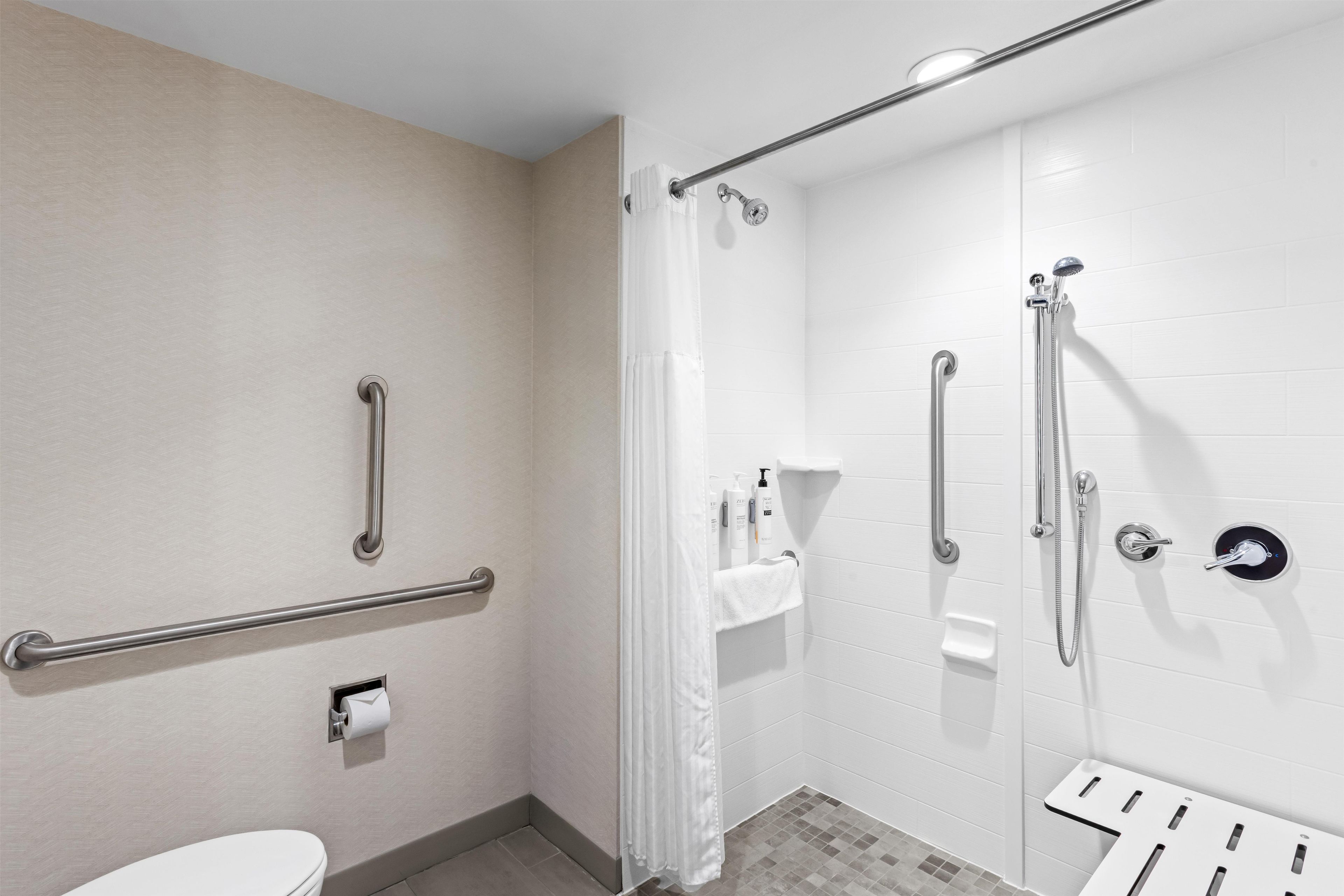 Un baño con inodoro, ducha con barras de apoyo y perchero.