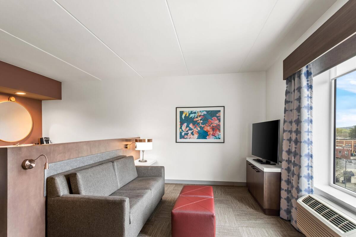 Ein Hotelzimmer mit Sofa, Flachbildfernseher, einem Gemälde und einem fenster mit Vorhängen.