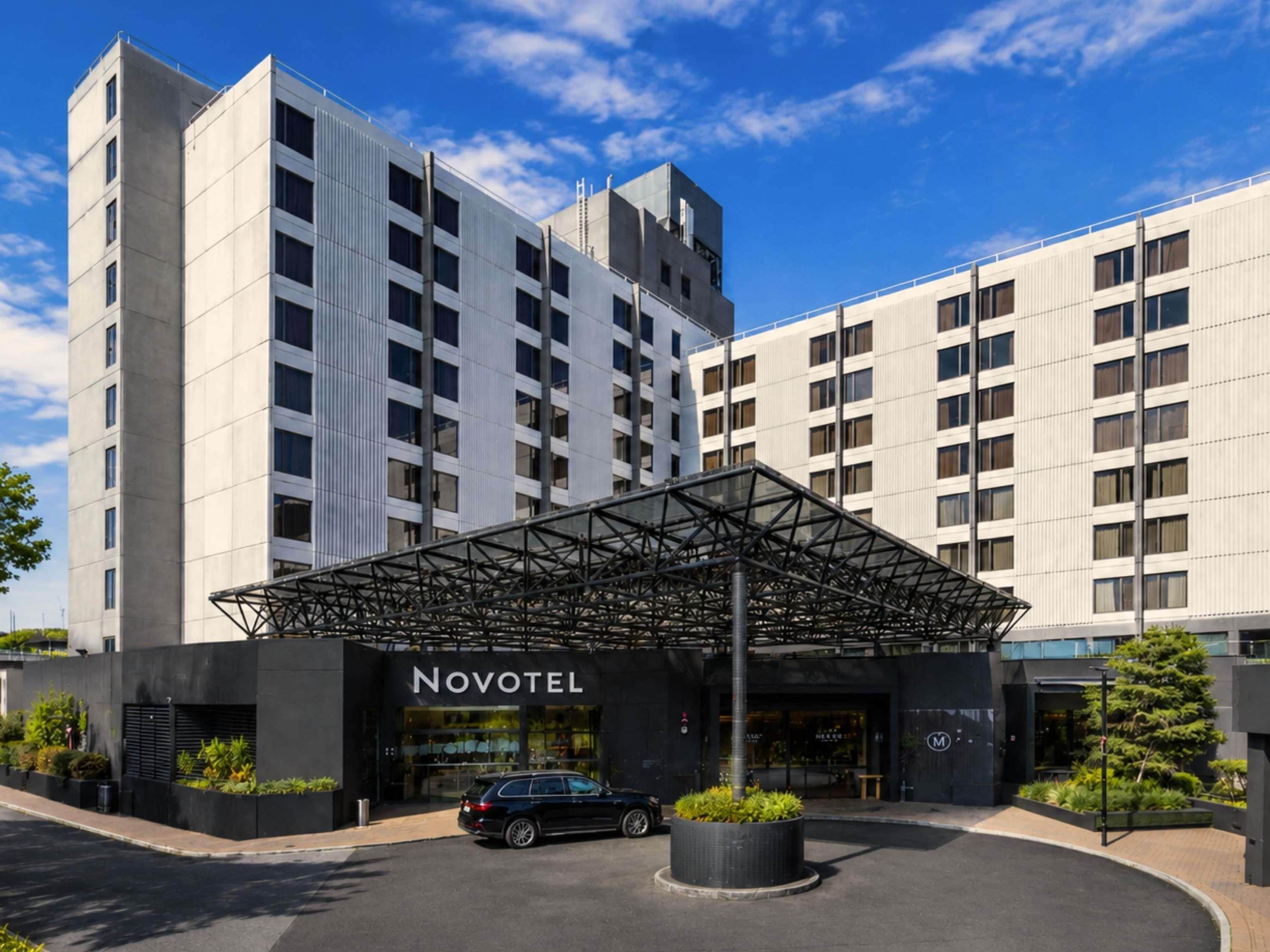 Un hotel con fachada moderna, un acceso cubierto y un área de estacionamiento.