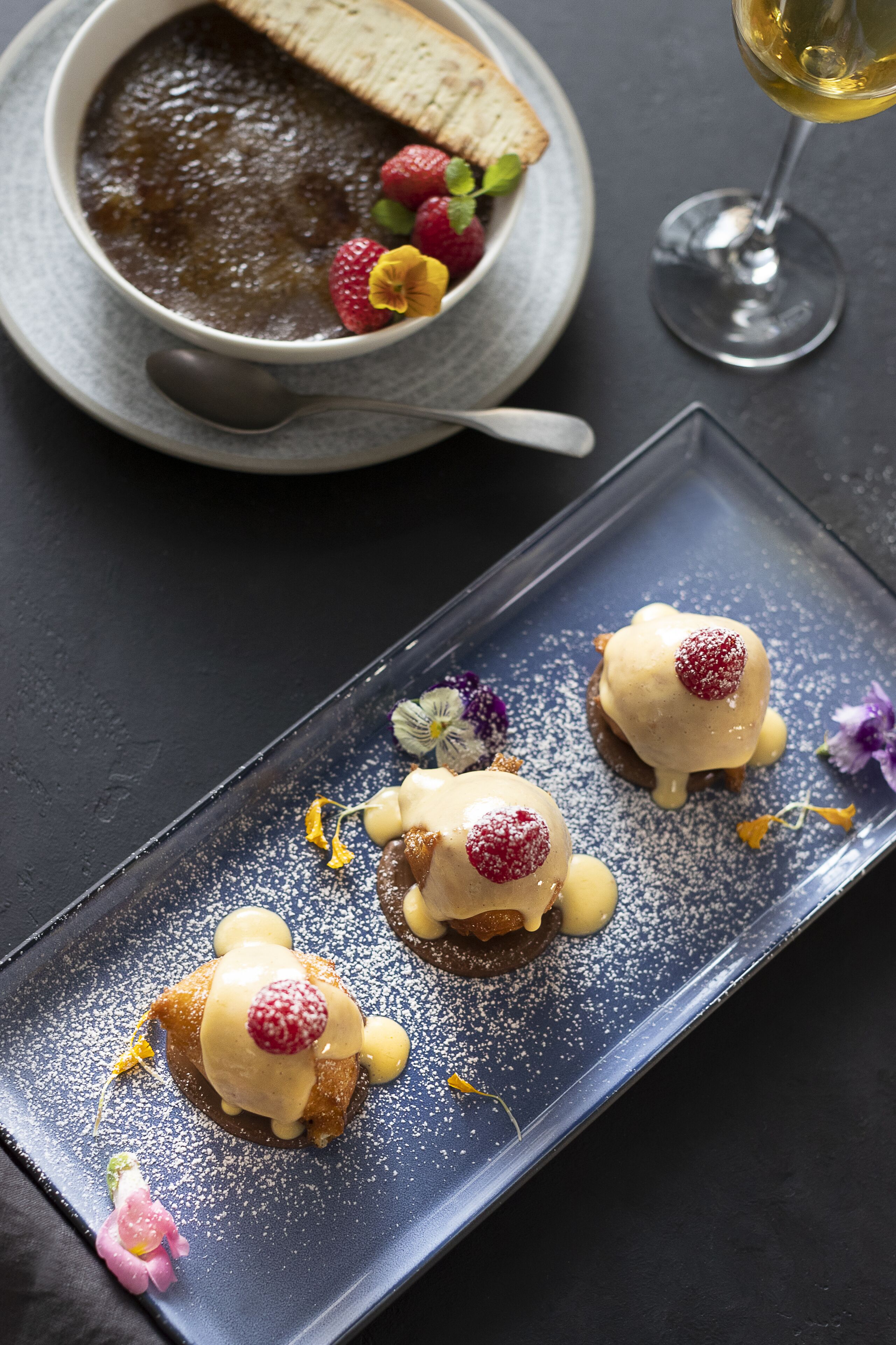 A dessert plate with three servings of chocolate mousse topped with strawberries and a glass of white wine.