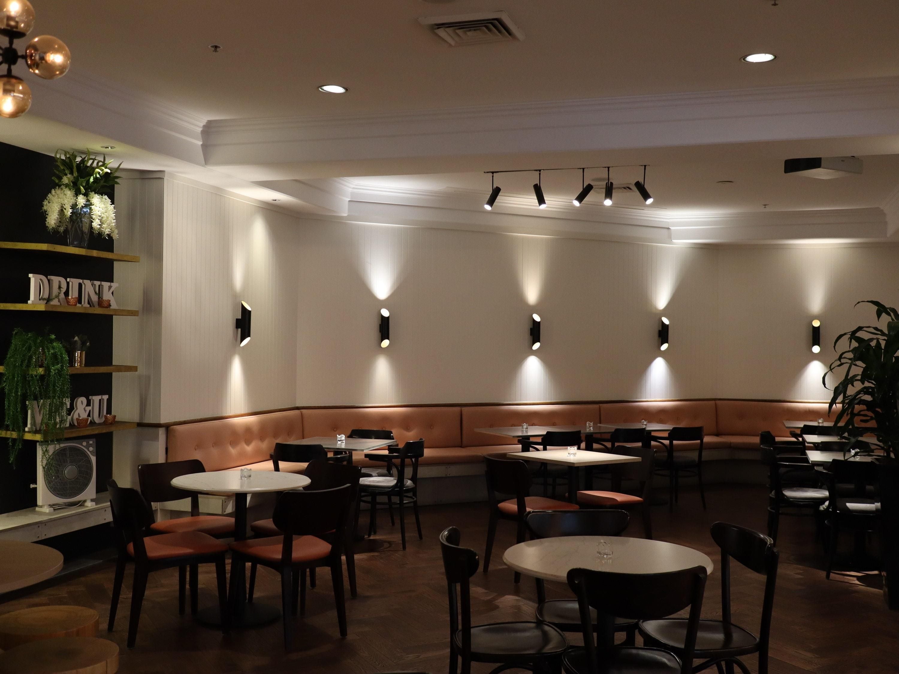 Un restaurant avec des tables rondes et des banquettes, un éclairage encastré et un ventilateur sur le côté gauche.
