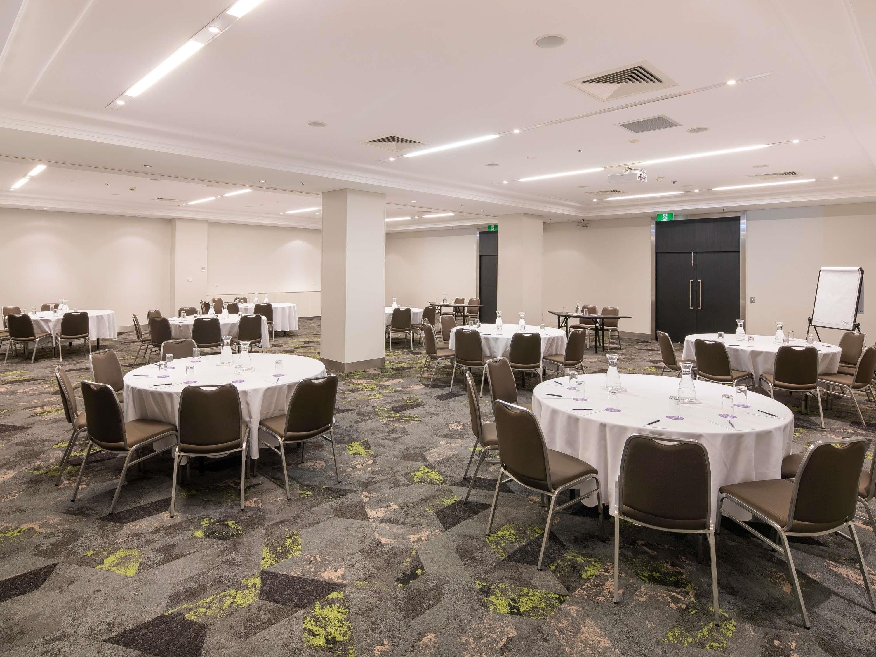 A conference room with multiple round tables, chairs, and a whiteboard.