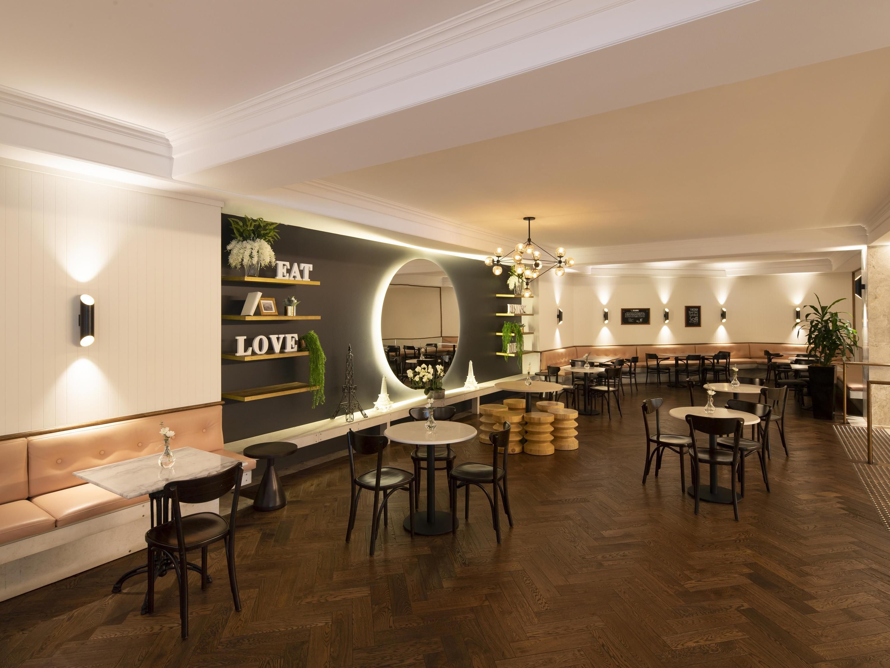Un restaurant amb interior modern, que destaca un mirall central, taules de fusta i una zona de seients amb un sofà.