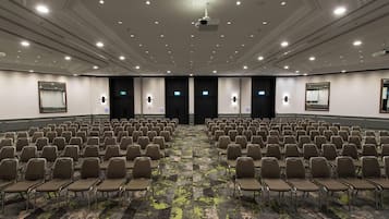 A large conference room with rows of chairs, a projector, and a carpeted floor.