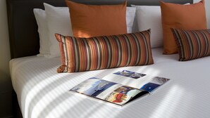 Una cama bien hecha con almohadones a rayas, una revista sobre la cama y un cabecero oscuro.