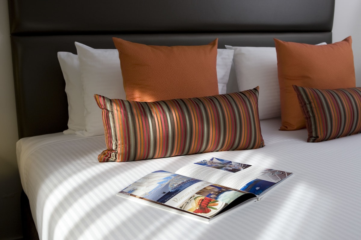 A neatly made bed with striped pillows, a magazine on the bed, and a dark headboard.