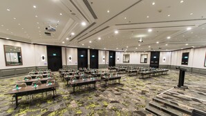 A large conference room with rows of tables and chairs, equipped with projectors and a stage. - Novotel Sydney International Airport Hotel (Wolli Creek)