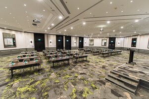 A large conference room with rows of tables and chairs, equipped with projectors and a stage.