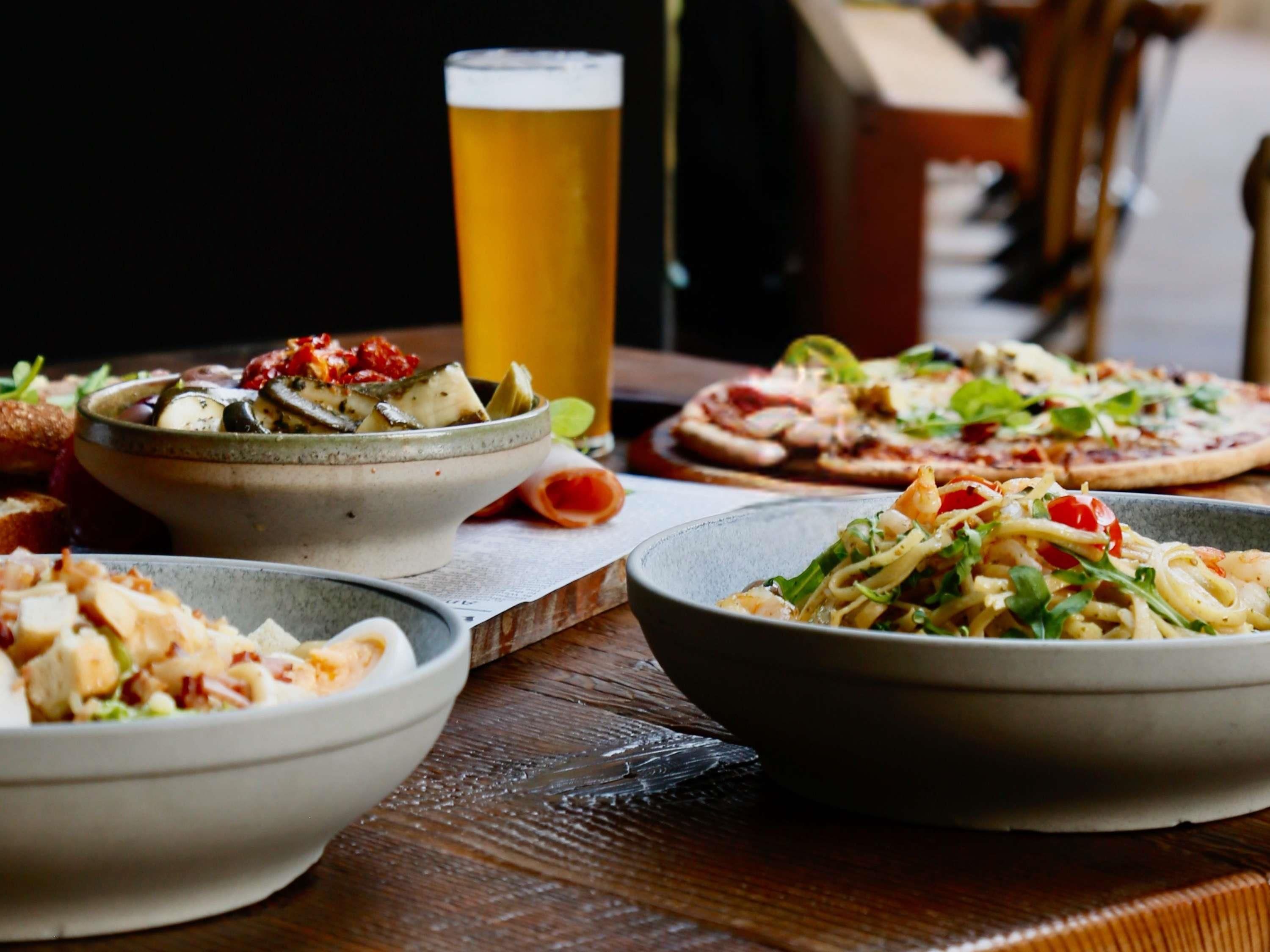 A dining table with various dishes, a glass of beer, and a rustic wooden table.