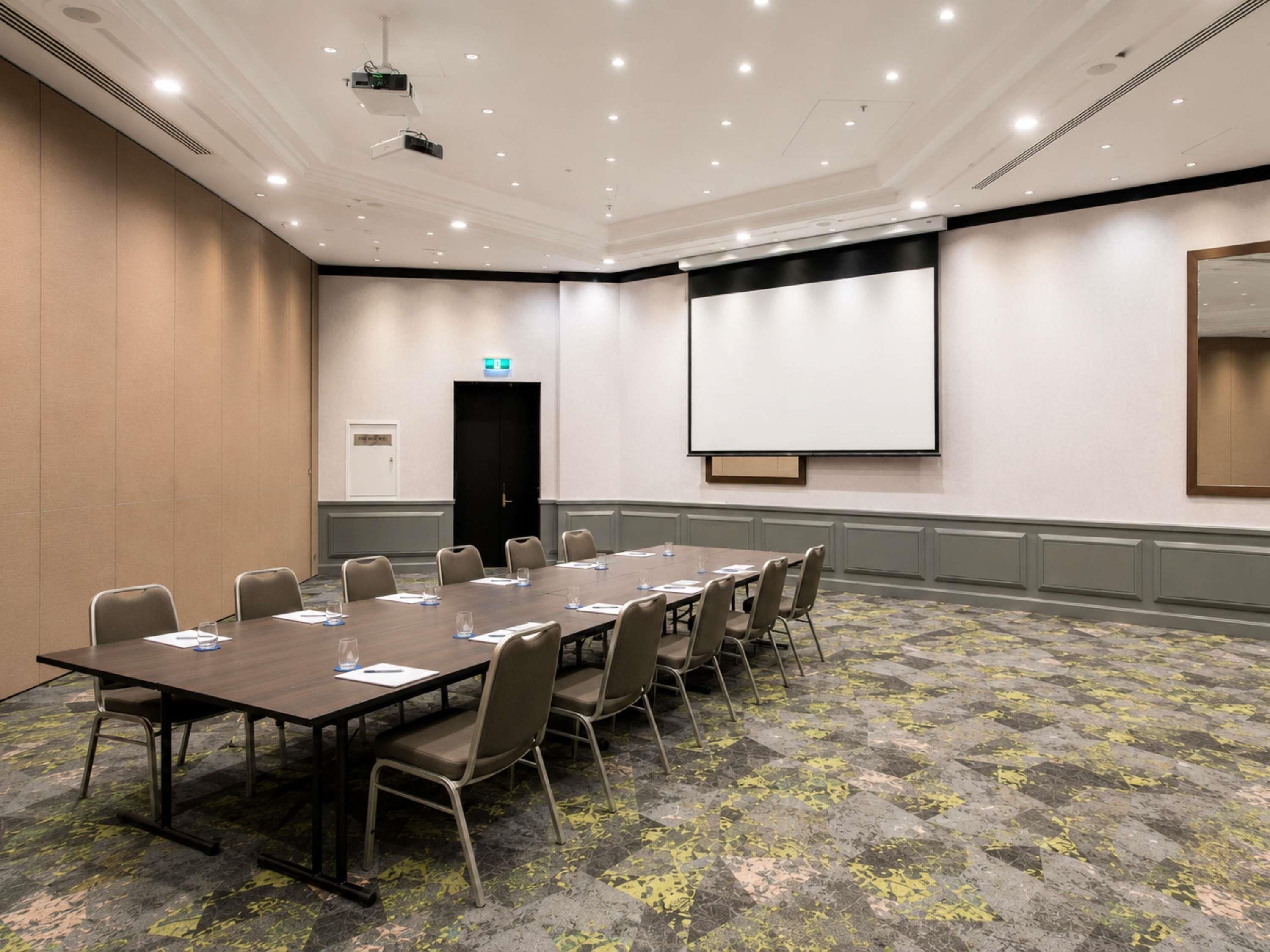 A conference room with a long table, chairs, a projector screen, and a door.