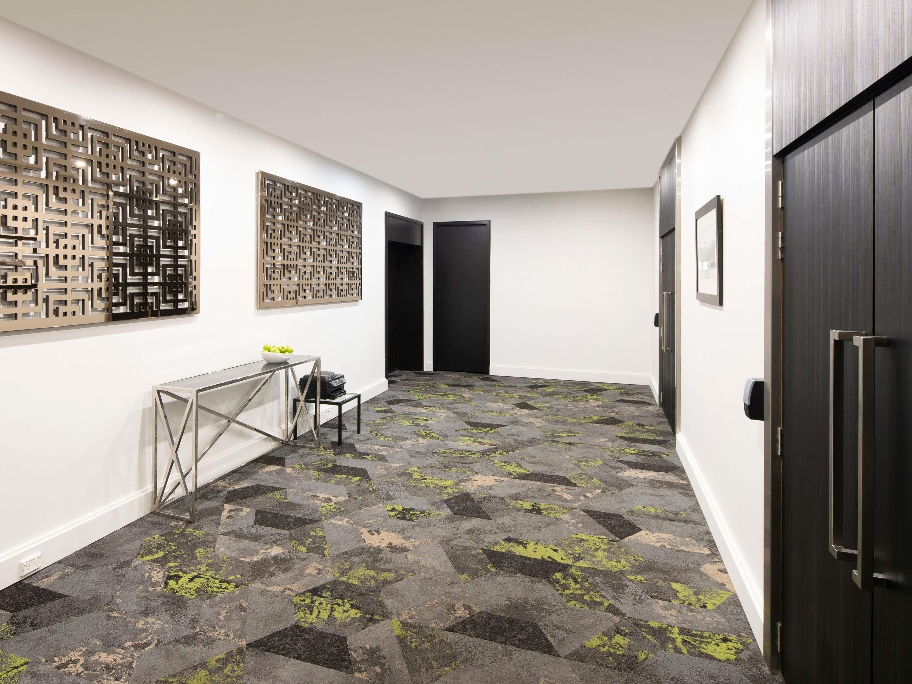 A hallway with a patterned floor, a desk with a bowl of fruit, and a door on the right.
