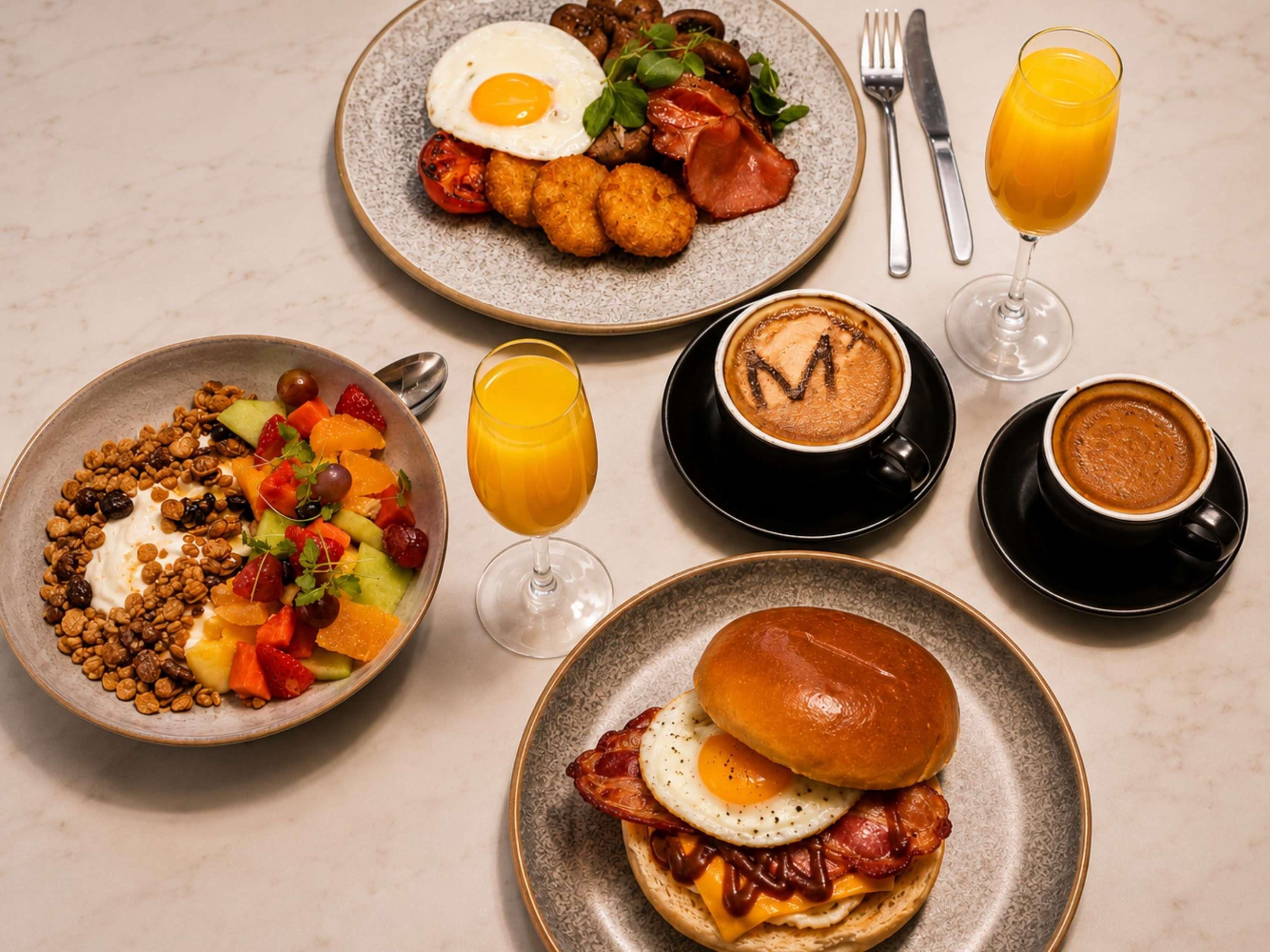 A breakfast setting with plates of food, glasses of orange juice, and coffee.