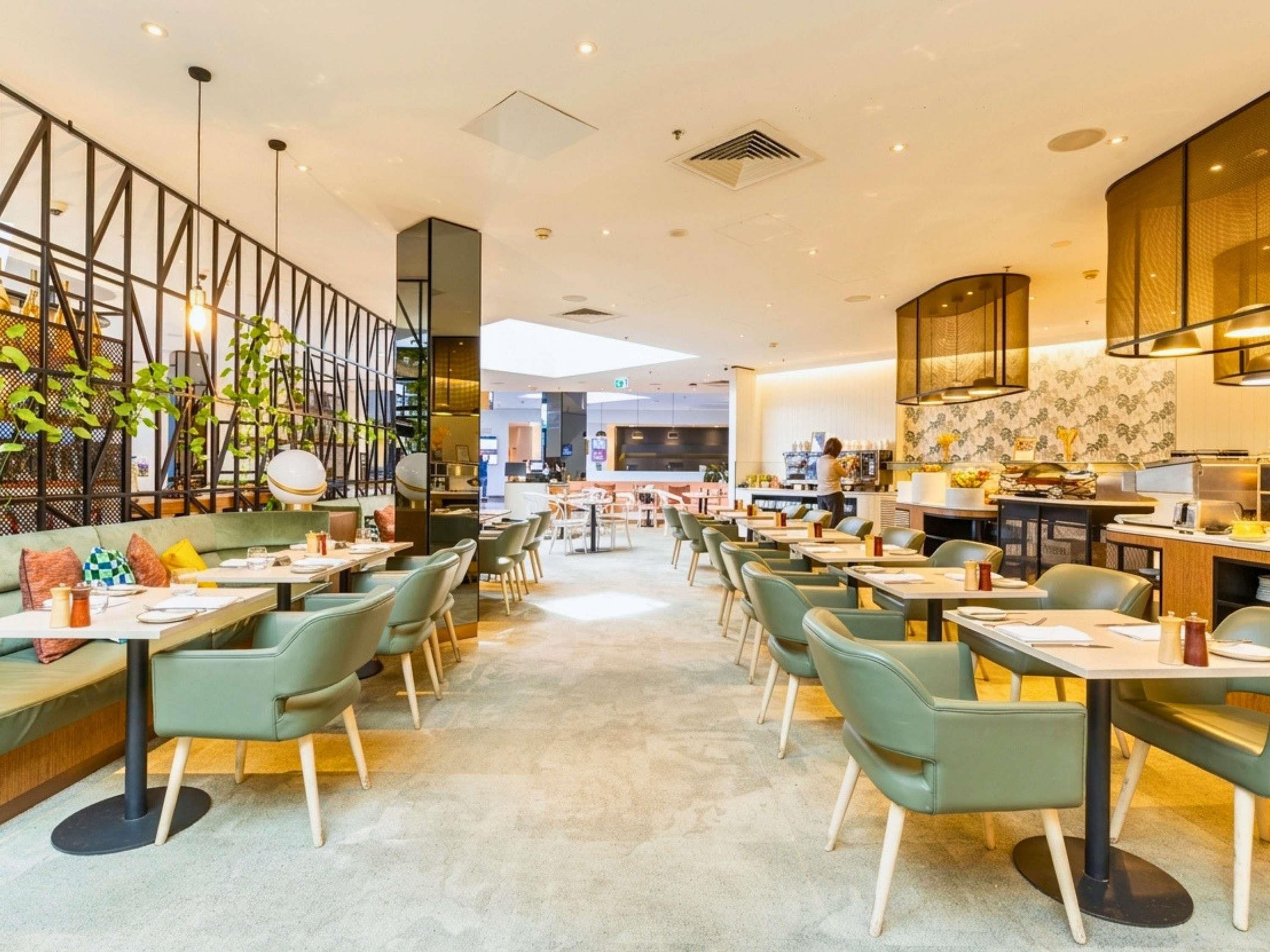 A modern restaurant interior with high tables and chairs, a bar area, and a view of the street.