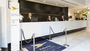 A hotel reception desk with a 'Priority Welcome' sign, online check-in options, and a reception area with a blue carpet. - Novotel Sydney International Airport Hotel (Wolli Creek)