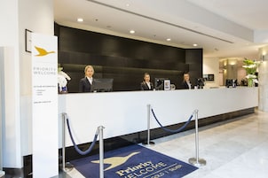 Un mostrador de recepción de hotel con un cartel que dice 'Priority Welcome', opciones de registro en línea y una zona de recepción con alfombra azul.