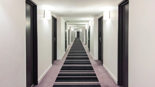 A long, narrow hallway with a black and white striped carpet, white walls, and doors on both sides. - Novotel Sydney International Airport Hotel (Wolli Creek)