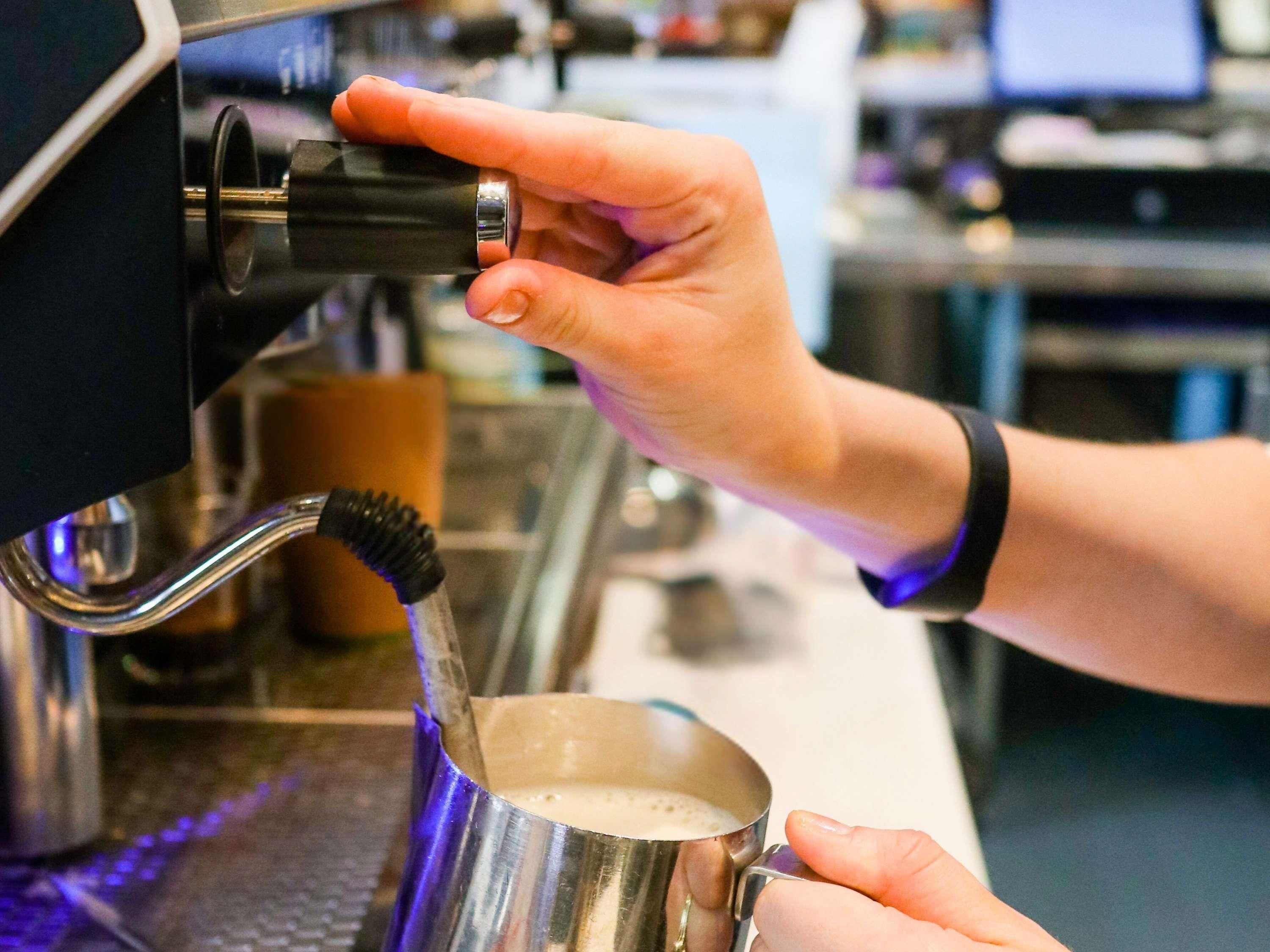 A person operating a coffee machine, with a metal cup placed under the spout.