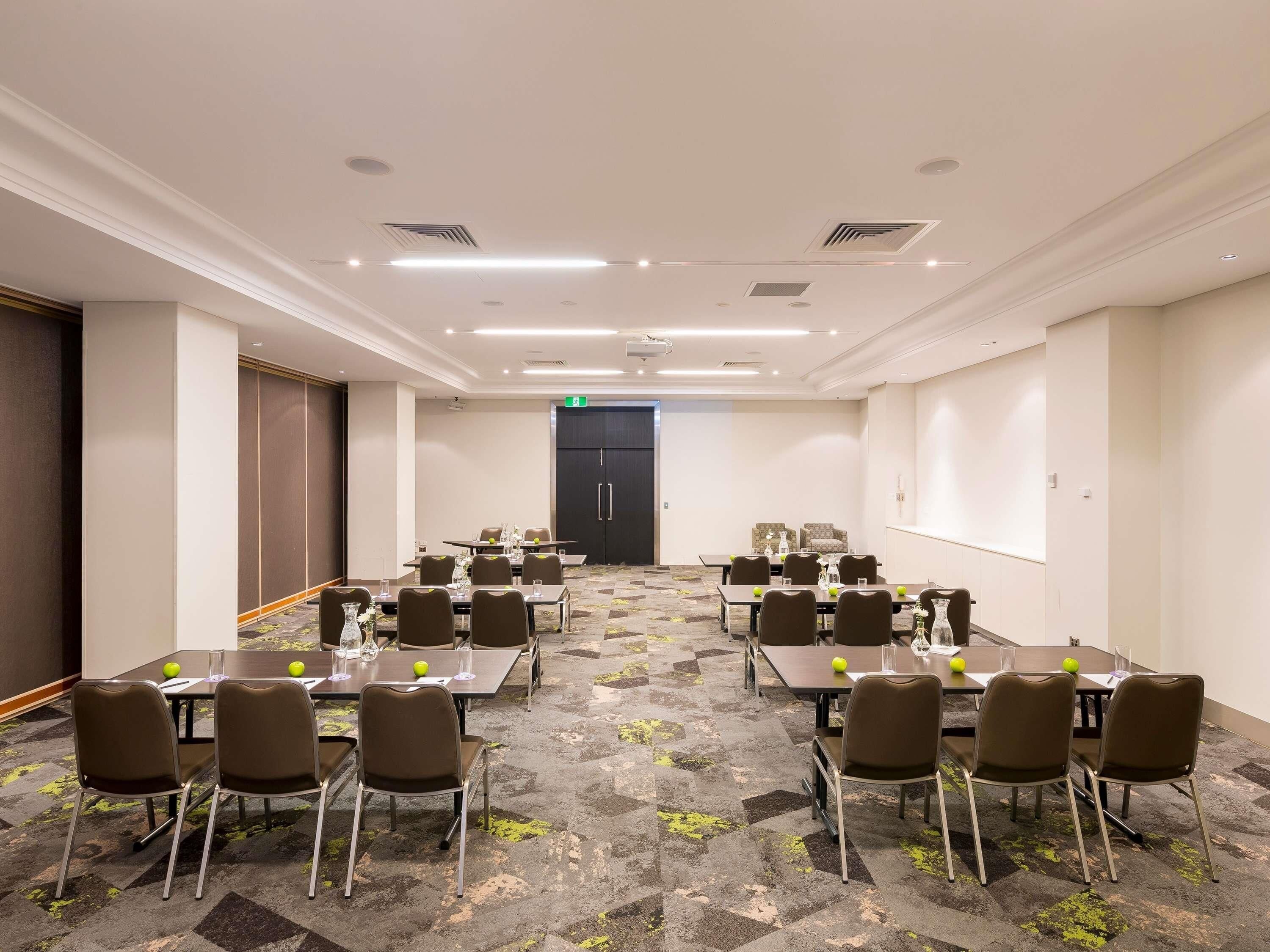 A conference room with multiple tables and chairs, a patterned carpet, and a door in the background.