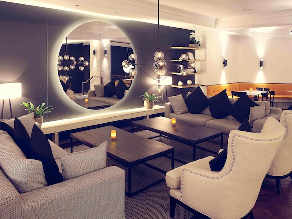 Una sala de estar moderna con un espejo grande, sofás, una mesa de centro y una estantería.