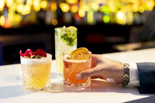 Un bar con dos bebidas, una con una rodaja de naranja y la otra con una rodaja de lima, y una mano sosteniendo una bebida.