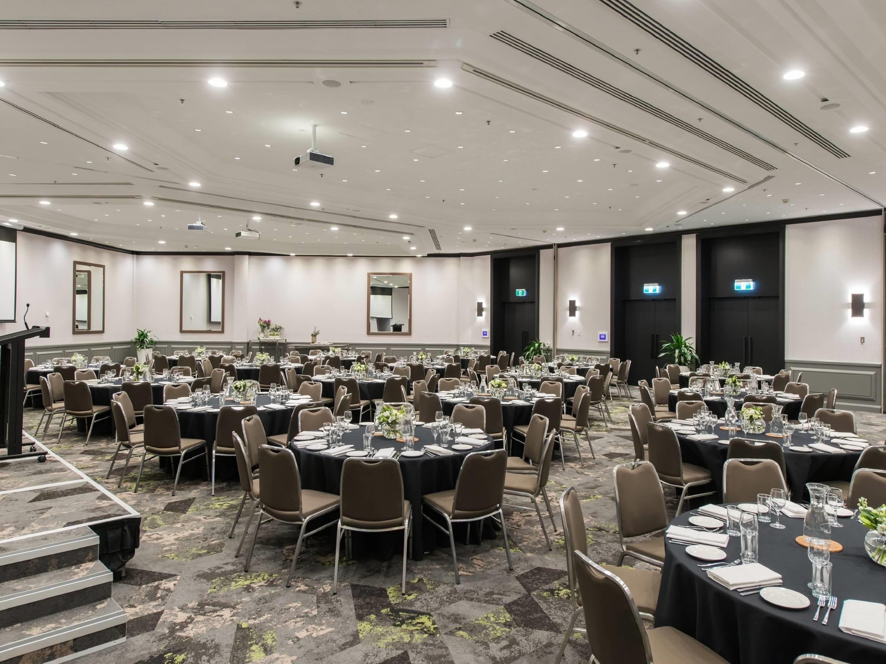 A large conference room with round tables, chairs, and a stage with a podium.